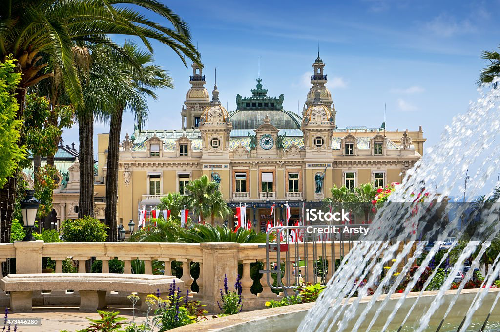 The ornate Belle Époque facade of the Casino de Monte-Carlo with its green-patina domes, framed by palm trees and a splashing fountain