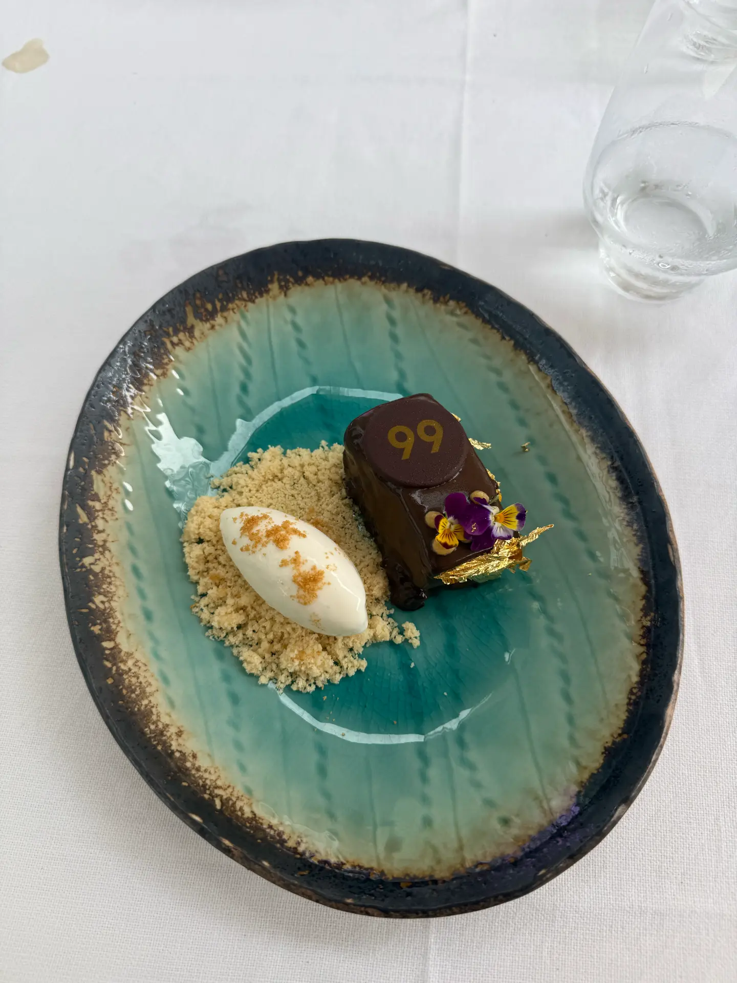 Chocolate dessert with cream quenelle, crumble, edible flowers and gold leaf at 99 Sushi Bar